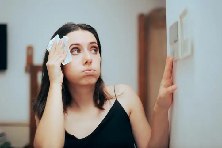 Woman feeling hot and adjusting her broken thermostat in Illinois